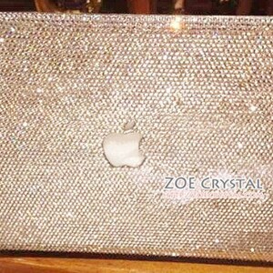 May include: A silver laptop cover completely covered in sparkling rhinestones. The Apple logo is visible in the centre of the cover. The text "ZOE CRYSTAL" is visible in the bottom right corner of the cover.
