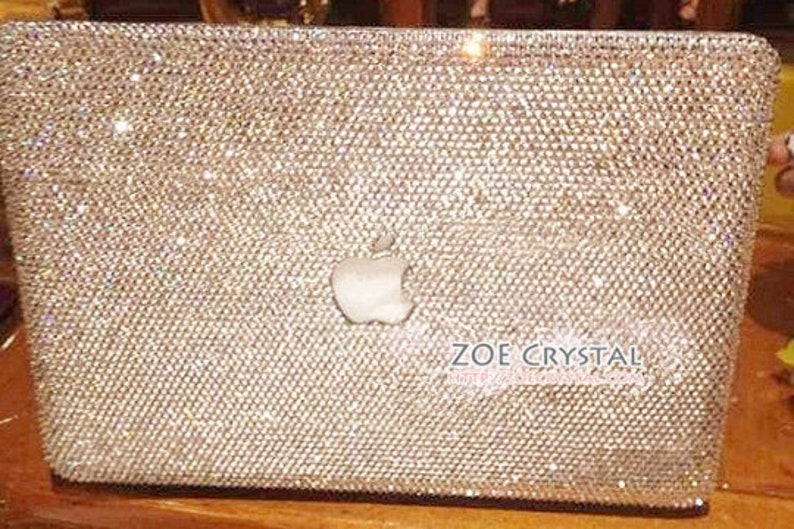 May include: A silver laptop cover completely covered in sparkling rhinestones. The Apple logo is visible in the centre of the cover. The text "ZOE CRYSTAL" is visible in the bottom right corner of the cover.