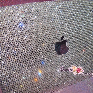 May include: A silver laptop covered in clear rhinestones with an Apple logo. The laptop has a website address printed on the bottom right corner: www.zoecrystal.com.