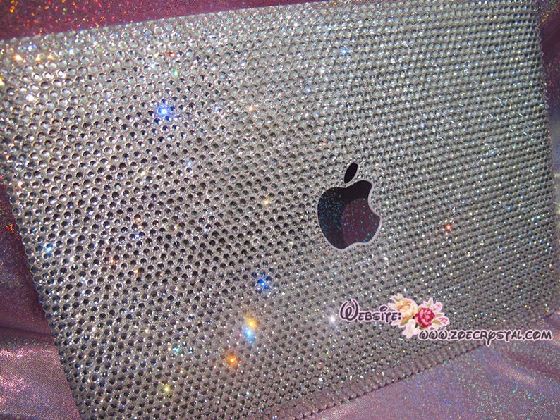 May include: A silver laptop covered in clear rhinestones with an Apple logo. The laptop has a website address printed on the bottom right corner: www.zoecrystal.com.