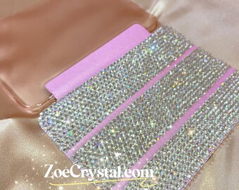 May include: A clear phone case with a pink backing and three horizontal rows of iridescent rhinestones.