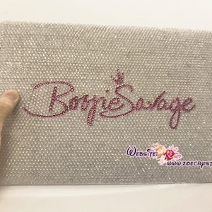 May include: A white, sparkly, rectangular surface with the words "Barbie Savage" in pink rhinestones. The text "Website: www.zoecrystal.com" is printed in black at the bottom.