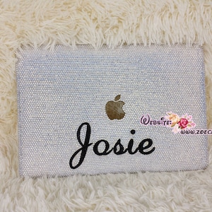 May include: A white laptop covered in clear rhinestones with a black cursive name "Josie" and a gold apple logo.