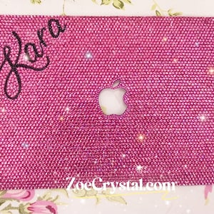 May include: Pink laptop case covered in rhinestones with the name "Kara" written in black lettering on the top left corner. The Apple logo is visible in the center of the case. The website "ZoeCrystal.com" is printed on the bottom of the case.