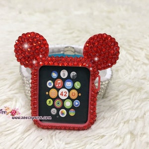 以下が含まれることがあります： ミッキーマウスの耳が付いた赤いラインストーンのアップルウォッチケース。ケースは赤いラインストーンで飾られており、透明な画面保護フィルムが付いています。時計の文字盤には時刻と日付が表示されています。