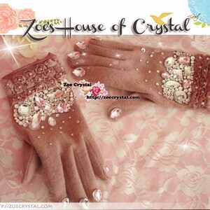 May include: A pair of pink fleece gloves with a floral design and embellished with rhinestones. The gloves are decorated with a variety of clear, pink, and white rhinestones. The text "Zoe's House of Crystal" is visible at the top of the image.