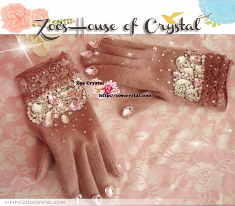 May include: A pair of pink fleece gloves with a floral design and embellished with rhinestones. The gloves are decorated with a variety of clear, pink, and white rhinestones. The text "Zoe's House of Crystal" is visible at the top of the image.