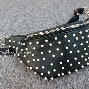 K&ouml;nnte beinhalten: Schwarze Bauchtasche mit wei&szlig;en perlenartigen Nieten und einem silbernen Kettenriemen. Die Tasche hat einen Rei&szlig;verschluss und einen schwarzen Riemen mit dem Text "ZoeCrystal.com".