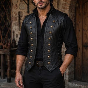 May include: A black leather waistcoat featuring two vertical rows of metallic gold buttons down the front, a high collar, and side lace-up detailing. The waistcoat is worn over a black long-sleeved shirt and black trousers with a dark leather belt.