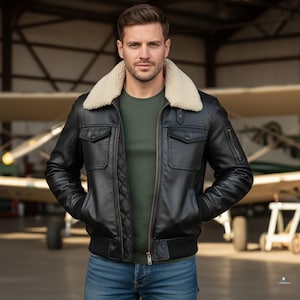 Puede incluir: Chaqueta de cuero negro con cuello de borreguillo color crema. La chaqueta tiene dos bolsillos en el pecho, dos bolsillos laterales y un patrón acolchado en la parte delantera. El modelo lleva una camiseta verde y vaqueros azules.