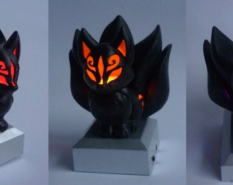 May include: A black, 3D printed figurine of a nine-tailed fox with glowing red, orange, and purple eyes. The figurine is on a small, silver base.