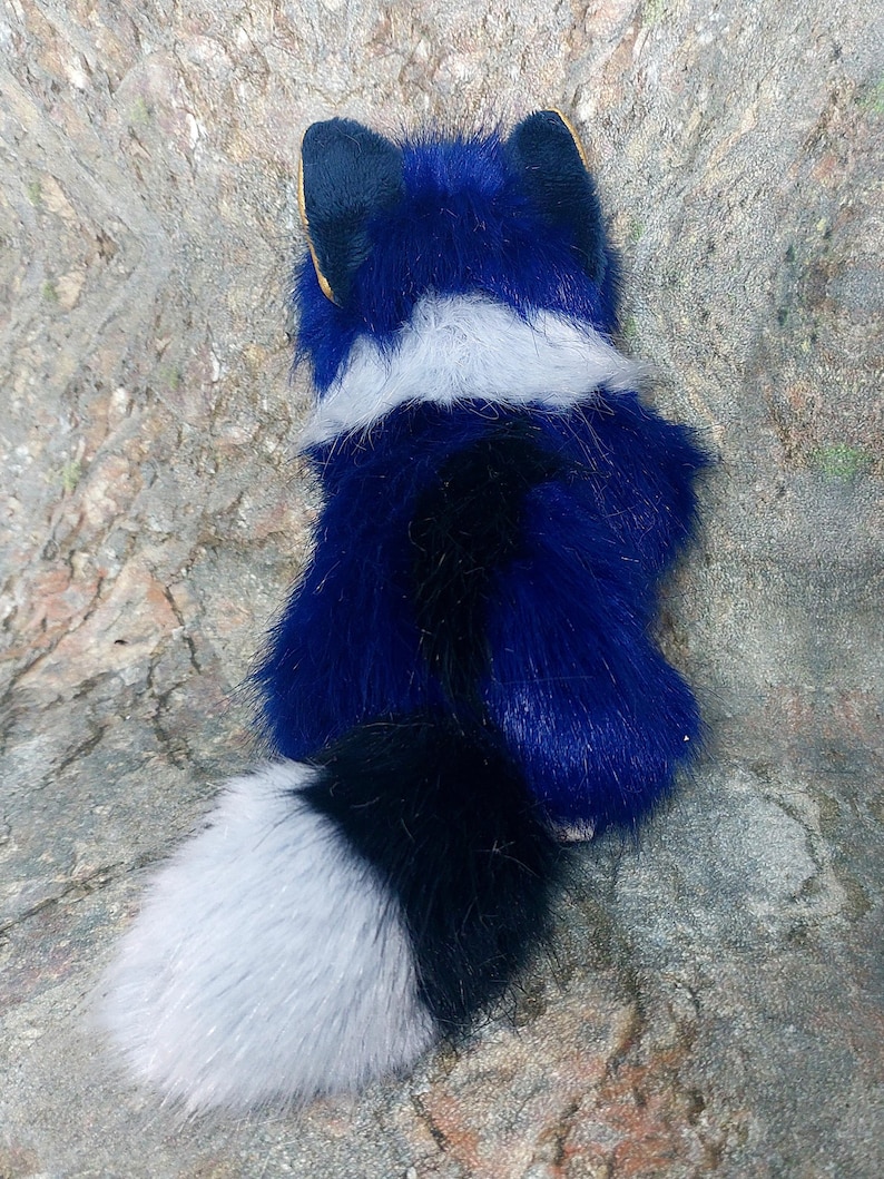 Puede incluir: Un juguete de peluche con forma de zorro de color azul, pecho blanco y cola negra y blanca.