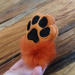 Può includere: Zampa di peluche arancione e nera con un pompon arancione soffice.