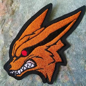 May include: Embroidered patch featuring an orange fox head with black accents and a red eye. The fox has a fierce expression with bared teeth, outlined in black. The patch has a black border.