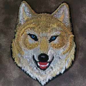 May include: Embroidered patch of a wolf's face with blue eyes and a red tongue. The wolf is depicted with a white and gold fur pattern.