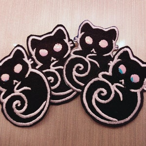 May include: Four black felt cat patches with white outlines and pink and blue eyes. The cats are curled up in a sleeping position.