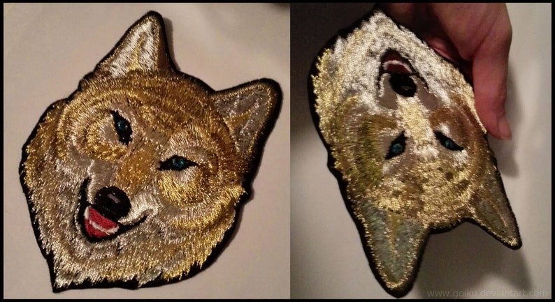 May include: Two embroidered patches of a wolf's head. The wolf has a light brown and white fur pattern with blue eyes. One patch is facing forward and the other is facing sideways.