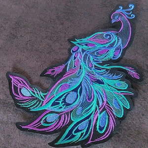 Peut inclure: Un patch brodé noir représentant un paon aux plumes bleues, vertes et violettes. Le paon est tourné vers la droite et sa tête est tournée vers la gauche.