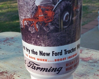 Puede incluir: Un vaso de acero inoxidable blanco con un anuncio vintage de un tractor Ford. El anuncio presenta un tractor rojo y naranja con el texto "Prueba la nueva forma de tractor Ford para ahorrar trabajo...Aumenta tus ingresos. La agricultura significa menos más ingresos."