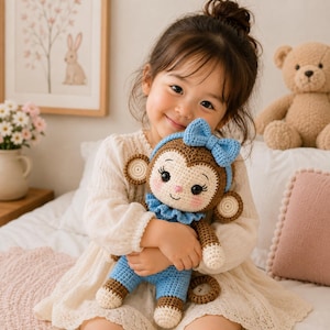 Pode incluir: Uma boneca de macaco em crochê com tons de castanho e creme, apresentando um colarinho com folhos azul-claro e um laço azul-claro a condizer na cabeça. A boneca tem traços faciais bordados, incluindo olhos escuros grandes com pestanas longas e bochechas rosadas.