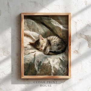 Puede incluir: Una impresión enmarcada que presenta un gatito durmiendo. El gatito tiene pelaje a rayas grises y marrones y está acurrucado sobre una manta estampada. El marco es de madera clara. El texto "CEDAR PRINT HOUSE" está en la parte inferior.