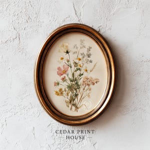 Peut inclure: Une impression encadrée ovale représentant un bouquet de fleurs sauvages roses, blanches et jaunes. L'impression est posée sur un fond crème et est encadrée dans un cadre doré. Le texte "CEDAR PRINT HOUSE" est en bas.