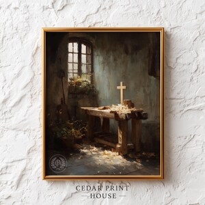 May include: A framed print of a workshop scene with a wooden cross on a workbench. The room has a window with light streaming in, illuminating the cross and wood shavings. The print is in a gold frame.