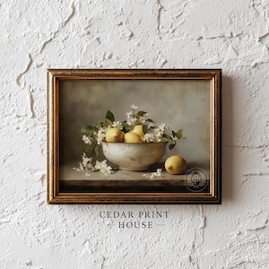 Op de afbeelding: Een ingelijst stilleven schilderij met een kom met citroenen en witte bloemen. De kom staat op een tafel met een donkere achtergrond. Het schilderij zit in een gouden lijst en heeft de tekst "CEDAR PRINT HOUSE" onderaan.