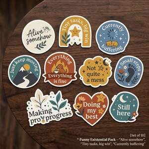 May include: A set of ten round and shaped stickers with motivational phrases and illustrations. Designs include a mountain scene, a sleeping cat, a paw print, and a heart with flowers. The stickers have a variety of colors and fonts.