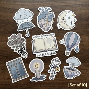 May include: Set of 10 stickers with a melancholic theme. Designs include a crying cloud with an umbrella, a heart, a moon, a bouquet of roses, an open book with the text "Melancholic yet Beautiful" and "Sad but Stylish", a hot air balloon, a window, a candle, a key, and a teacup.
