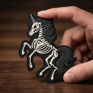 May include: A black and white rubber patch featuring a rearing unicorn skeleton design. The unicorn has a dark black mane and tail, a white skeletal structure, and a single horn on its head. The patch is shaped to follow the outline of the unicorn.