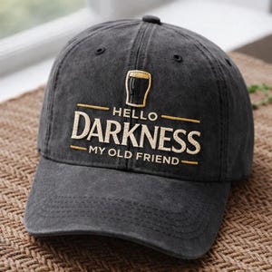 以下が含まれることがあります： 「Hello Darkness My Old Friend」の金色の刺繍が施された濃いグレーの野球帽。 デザインには、テキストの上にビールのグラスのアイコンが含まれています。