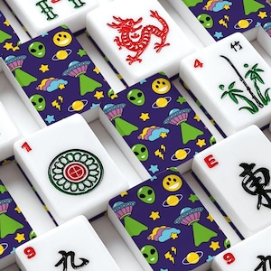 May include: A collection of white mahjong tiles featuring traditional red, green, and black symbols, interspersed with tiles displaying a dark purple pattern of green alien faces, colorful UFOs, yellow stars, and planets on a white background.