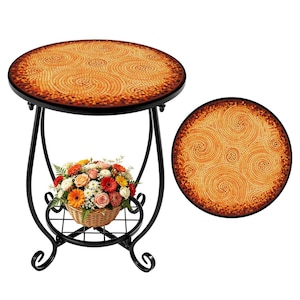 May include: A round mosaic tile top side table with a black metal frame. The tabletop features a spiral design in shades of orange and brown. A wicker basket filled with flowers sits on a lower shelf. The table is approximately 24 inches in diameter.