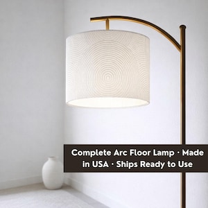 May include: An arc floor lamp with a white drum shade featuring a circular pattern. The lamp has a bronze-colored metal frame and a curved arm. The text on the image says "Complete Arc Floor Lamp".