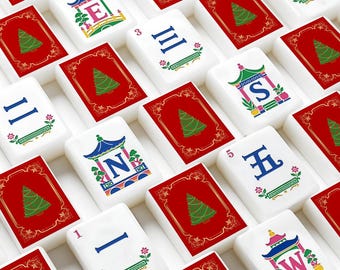 May include: A collection of rectangular mahjong tiles arranged in a grid. Some tiles feature a red background with a green Christmas tree illustration, while others are white with blue Chinese characters, numbers, or letters E, S, N, W.