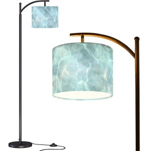 May include: A black arc floor lamp with a cylindrical lampshade. The lampshade features a blue and white water-like pattern. The lamp has a black base and a gold-colored curved arm. The lamp is plugged into a wall outlet.
