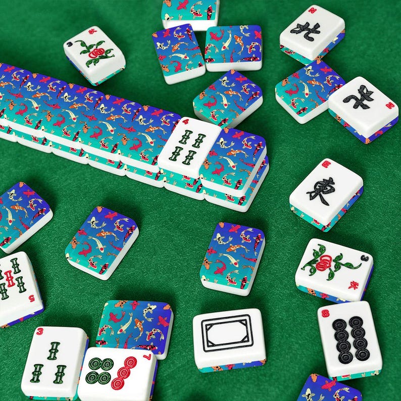 May include: A collection of Mahjong tiles scattered on a green surface. The tiles are white with various symbols and designs, including koi fish patterns in blue and red. Some tiles have Chinese characters.