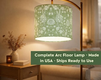 May include: An arc floor lamp featuring a cylindrical lampshade with a sage green and white botanical floral pattern. The lamp has a curved metal stand and emits a warm light. The text on the image reads Complete Arc Floor Lamp.