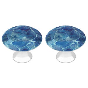 May include: Two circular cake stands featuring a vibrant blue and white water ripple pattern on the flat top surfaces. Each stand is supported by a solid, smooth, silver-colored pedestal base that flares slightly toward the bottom for stability.
