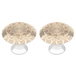 May include: Two round cabinet knobs featuring a beige and cream mandala pattern on the top surface. Each knob has a circular face with intricate floral and geometric line work and a smooth, silver-toned metal base that tapers toward the bottom.