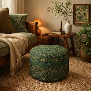 May include: A round, upholstered ottoman with a floral pattern in shades of green, blue, and yellow. The ottoman sits on a woven jute rug, and is near a wooden sofa with pillows and a throw blanket.