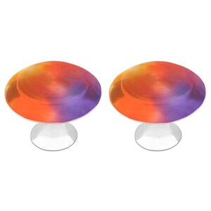 May include: Two cabinet knobs featuring a circular top with a gradient finish transitioning from vibrant orange to deep purple. Each knob has a smooth, metallic surface on the top and a solid, silver-colored cylindrical base for mounting.
