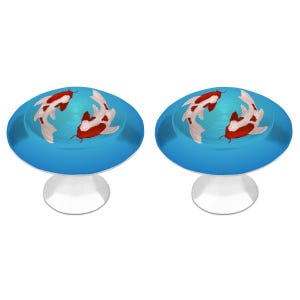 May include: Two round cabinet knobs featuring a vibrant blue background with a graphic illustration of two koi fish in red and white. Each knob has a smooth, domed surface and a silver-toned metal base, designed for attachment to furniture drawers.