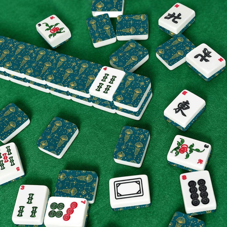 May include: A collection of Mahjong tiles scattered on a green surface. The tiles are white with various symbols and numbers, and some have a teal and gold pattern. The game pieces are arranged in a visually appealing manner.
