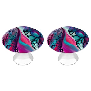 May include: Two round knobs featuring a vibrant fluid acrylic pour design with swirling patterns of magenta, deep purple, teal, and black. Each knob has a smooth, glossy surface and is mounted on a simple, solid silver-toned metal base.