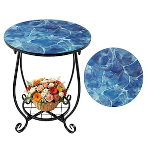 May include: A round side table with a blue water-like pattern on the tabletop. The table has a black metal frame with a lower shelf and decorative scrollwork. A wicker basket filled with colorful flowers sits on the shelf.