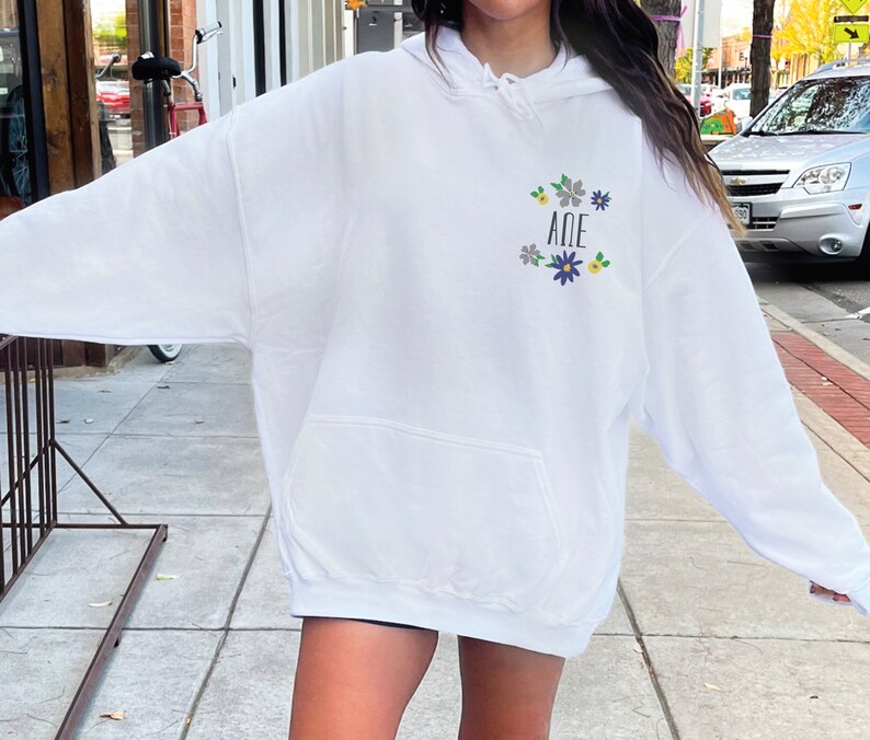 May include: White hooded sweatshirt with a purple and yellow floral design and the letters "A&Delta;E" in the center.