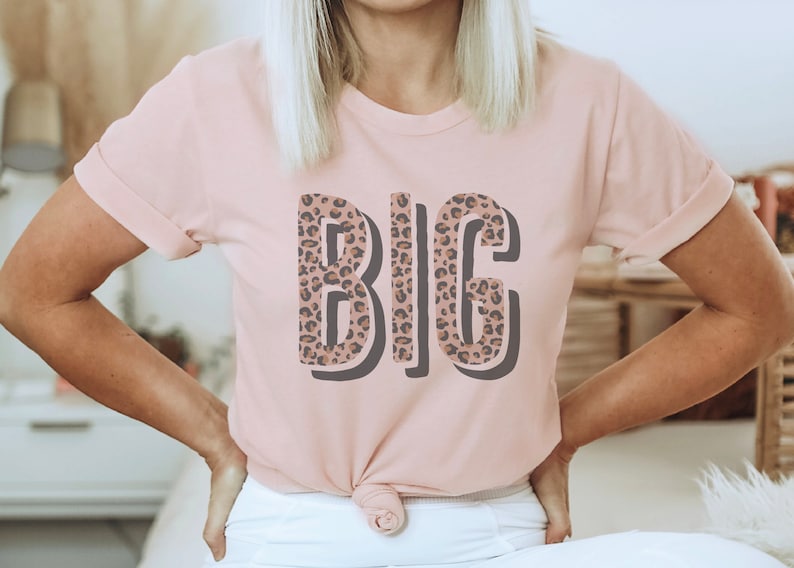 May include: A pink t-shirt with the word "BIG" printed on it in a leopard print pattern.