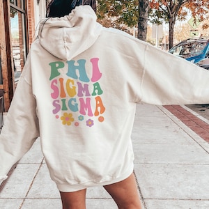 May include: A white hoodie with a colourful retro-style graphic on the back that says "Phi Sigma Sigma" with flowers.